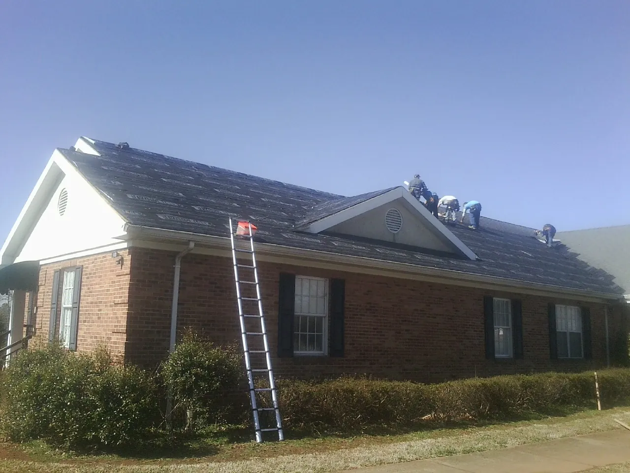 Crew tearing shingles off a brick ranch roof with a ladder set — Emergency Roof Repair work by our crew in East Brady