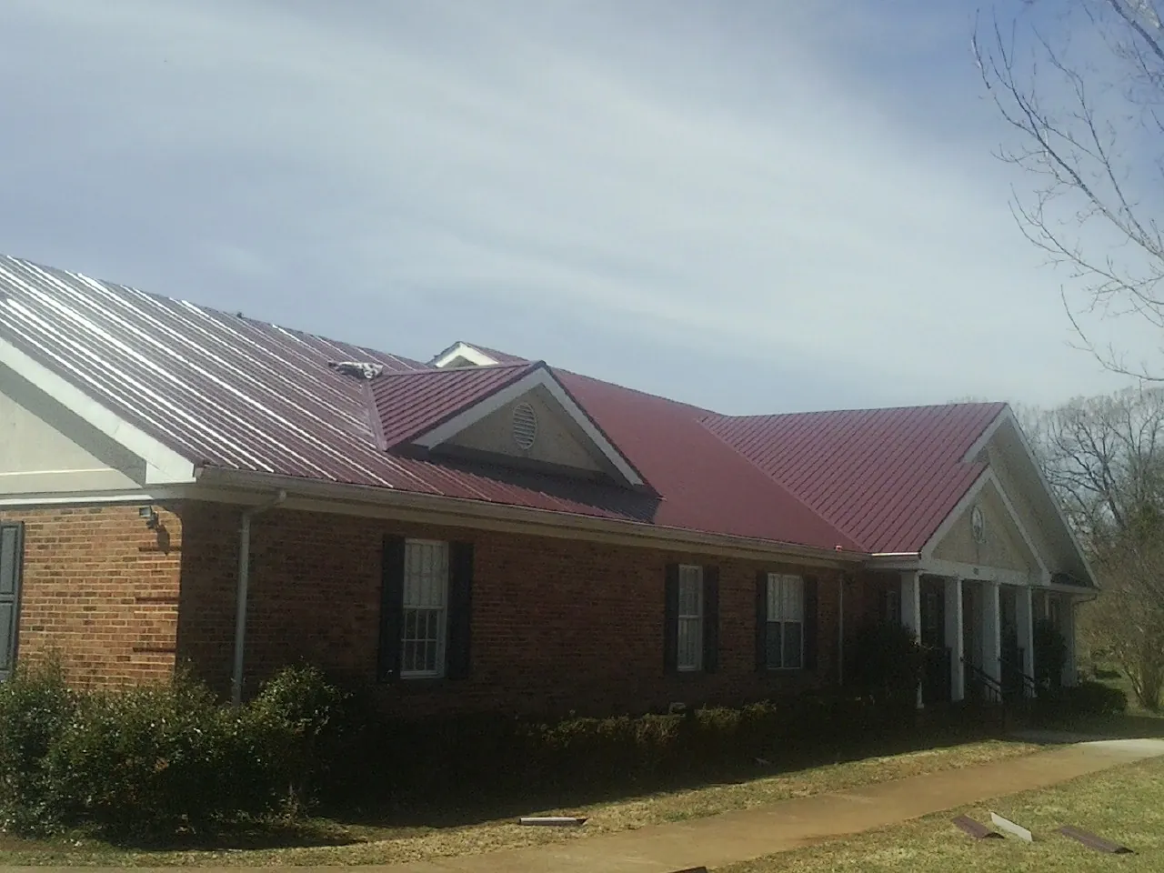 Red metal roof with gabled entries on a long brick building, from a Hail Damage Roof Repair job in East Brady