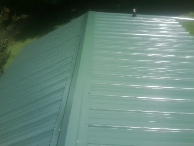 New green metal panels meeting at the ridge of a roof — Flat Roof Repair work by our crew in East Brady