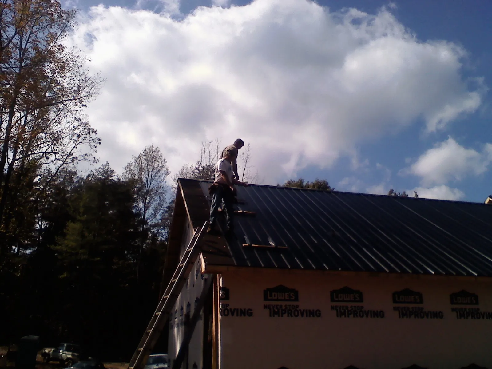 Roofer fastening dark metal panels high against a cloudy sky, from a Roof Inspection job in East Brady