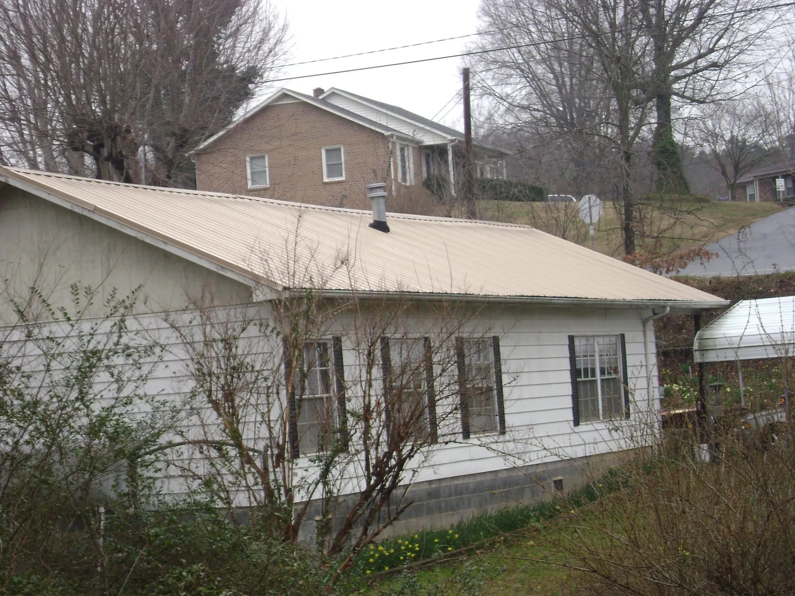 Tan metal roof on a white sided house set into a hillside — Commercial Roofing by Roofing Brothers in East Brady